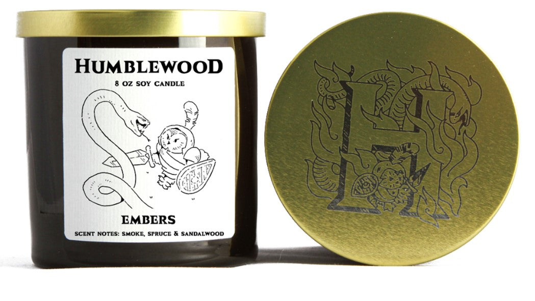 Dark Humblewood candle with a gold lid. The label shows an owl knight fighting a snake. The lid is etched with an "H" and dragon.