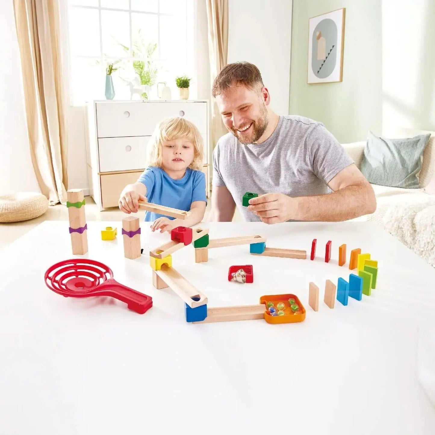 Father and child building the wooden Crazy Rollers track set with colorful blocks, ramps, marbles, and a curved line of vibrant dominoes
