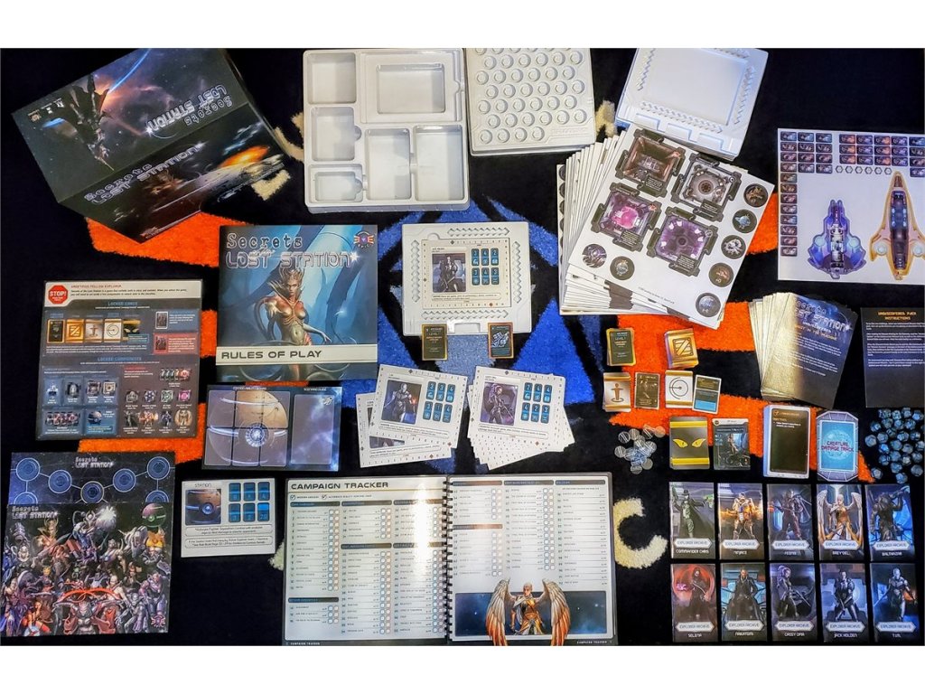The Secrets of the Lost Station board game is displayed spread out on a dark surface, showing its box, rulebook, game boards, cards, tokens, dice, and campaign tracker