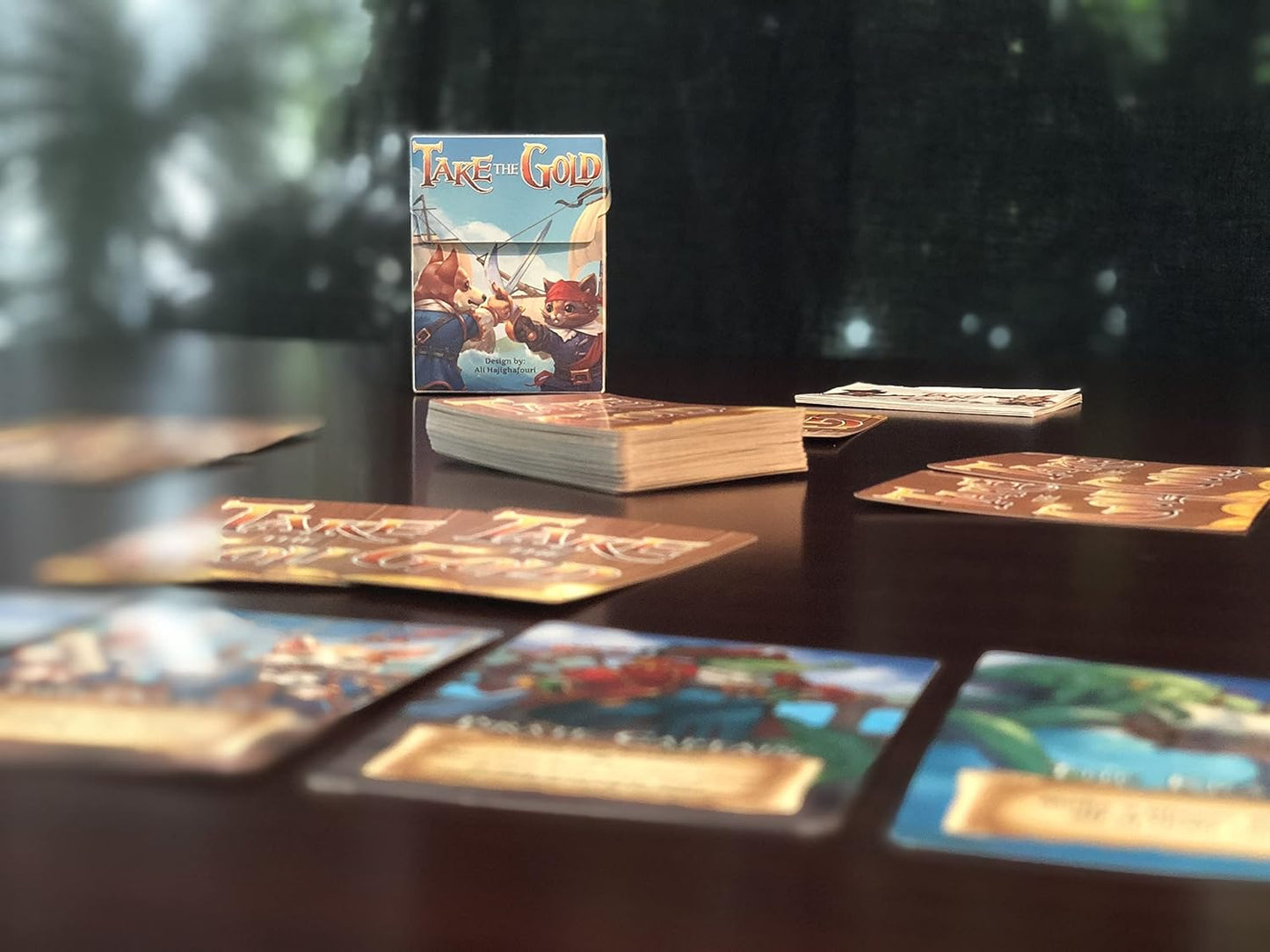 Take the Gold card game box, showing anthropomorphic pirate art, with scattered cards on a dark table.