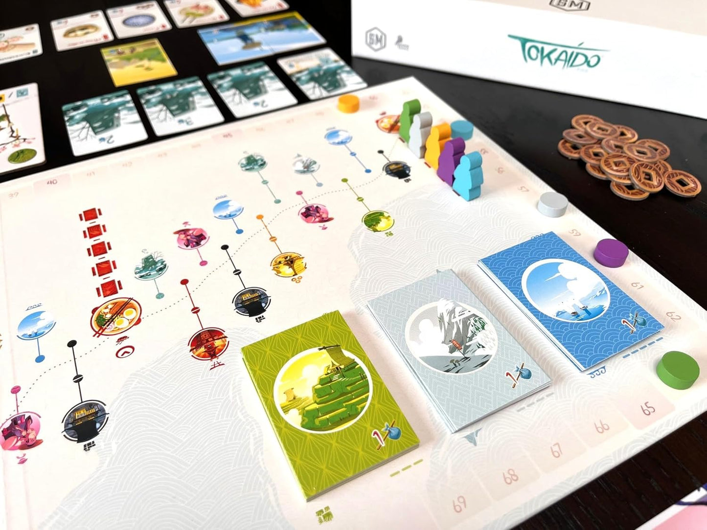 Tokaido board game setup showing the path, colorful traveler meeples, stacks of cards, and money tokens