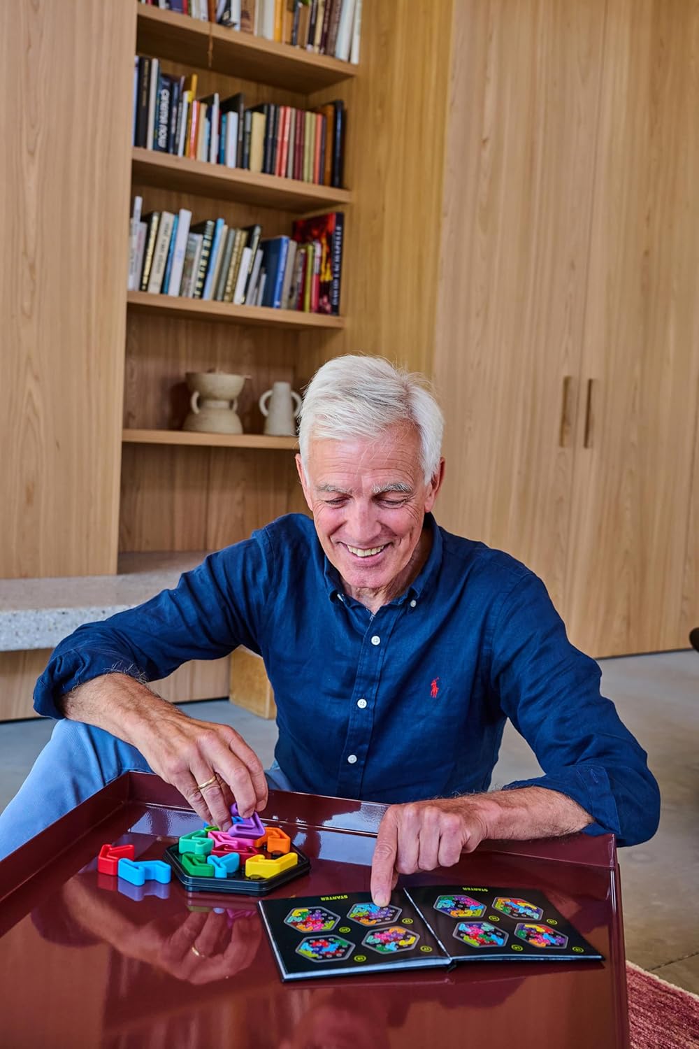 Older man smiling while playing a colorful logic puzzle game indoors