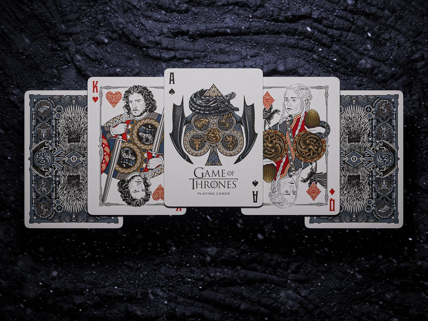 Game of Thrones playing cards displayed face-up (King, Queen and branded Ace) on a dark, textured surface