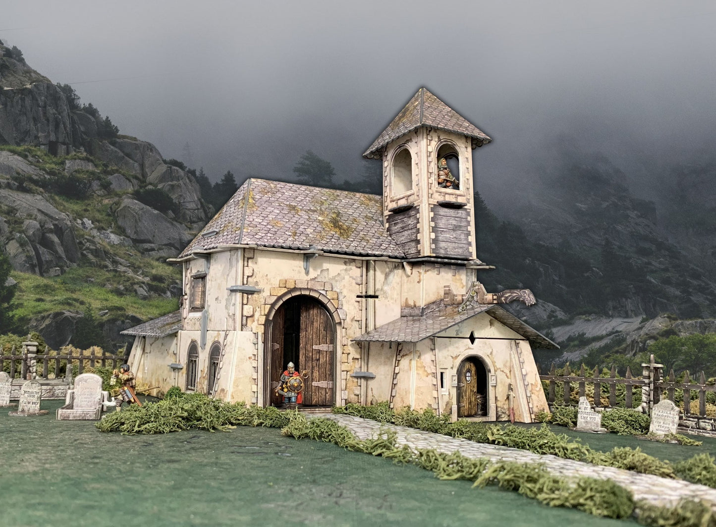 Miniature diorama: Weathered church with figures in doorway, bell tower, and graveyard. Misty mountains background.