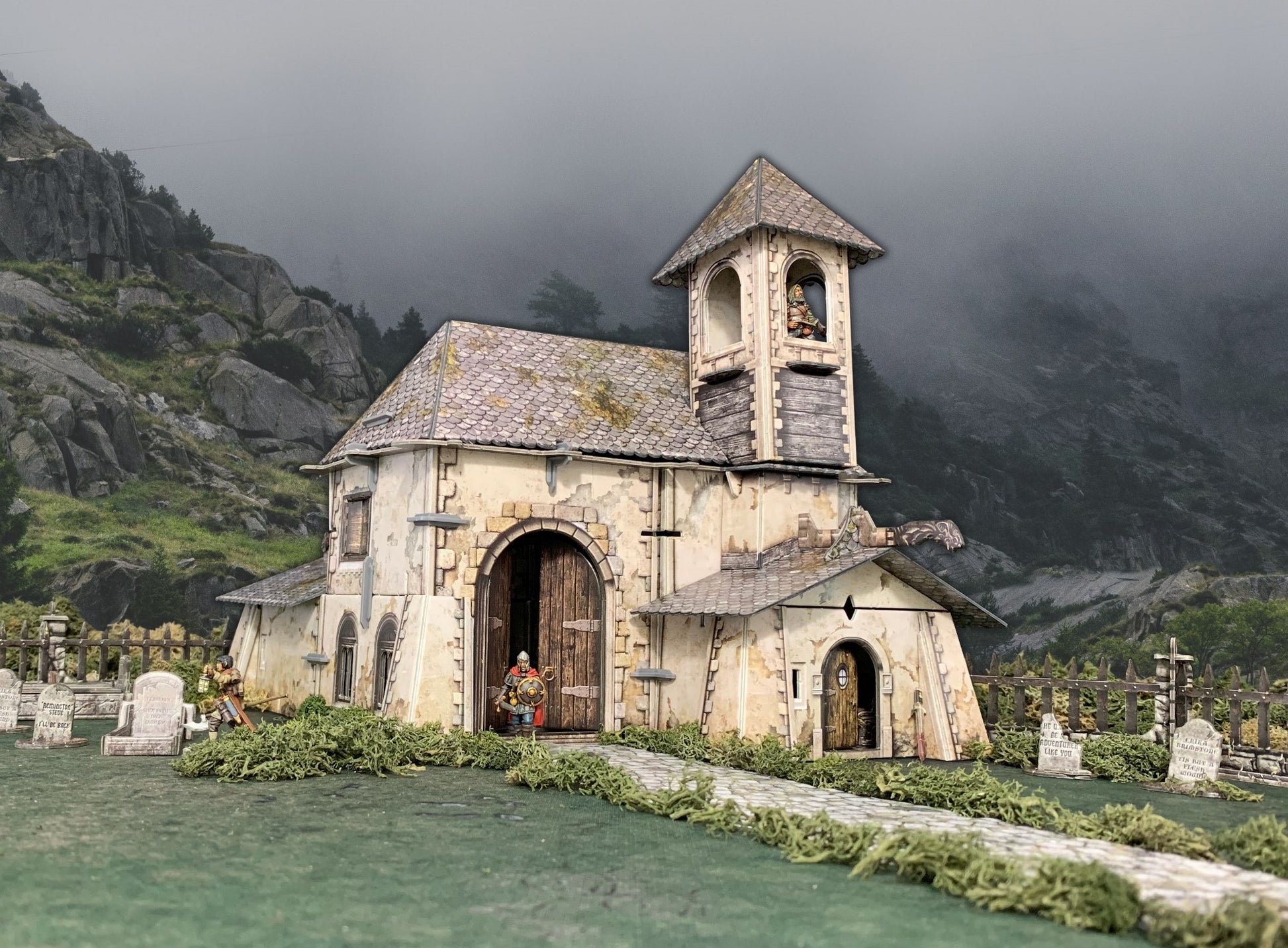 Miniature diorama: Weathered church with figures in doorway, bell tower, and graveyard. Misty mountains background.