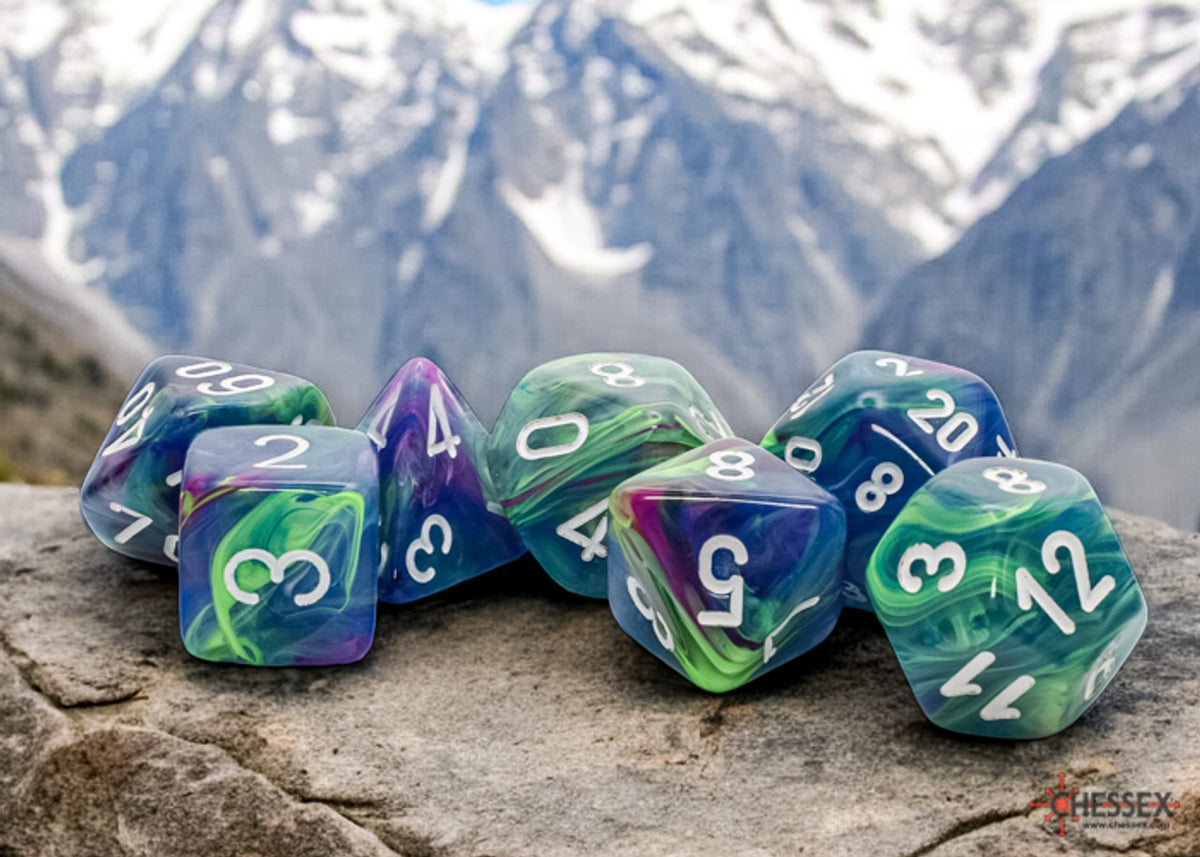 A set of green, blue and purple swirled polyhedral dice rests on a rock with snowy mountains behind