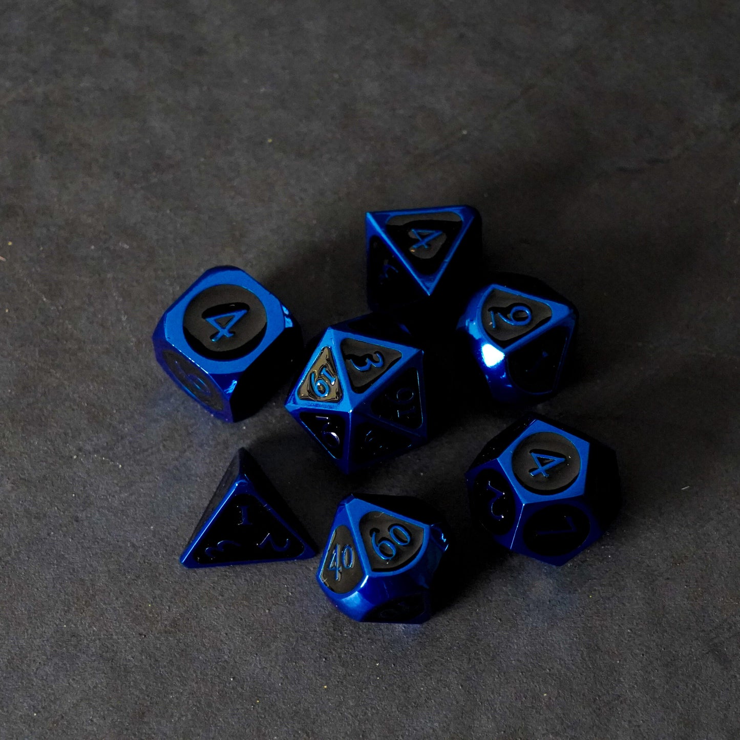 A set of seven metallic blue and black polyhedral dice scattered on a dark textured background.