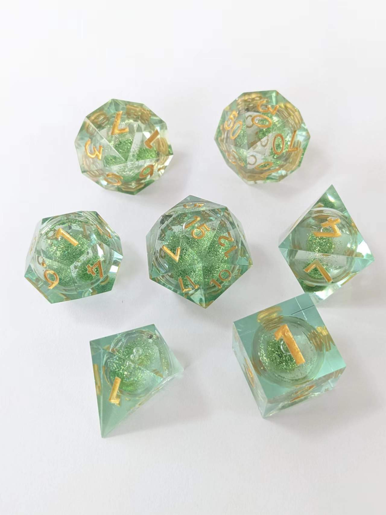 Seven clear green glitter dice with gold numbers, scattered on a white background