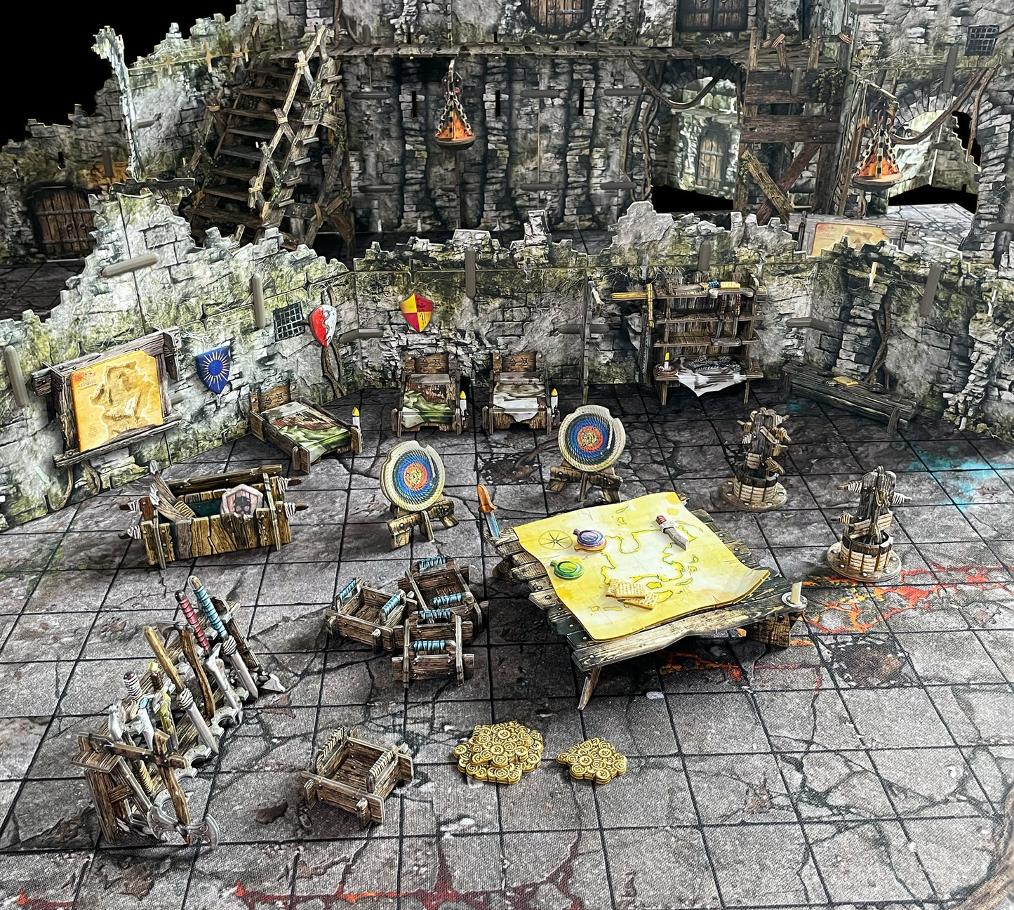 A miniature tabletop RPG dungeon setup with stone walls, stairs, beds, a map, weapon racks, and gold coins on a grid mat.