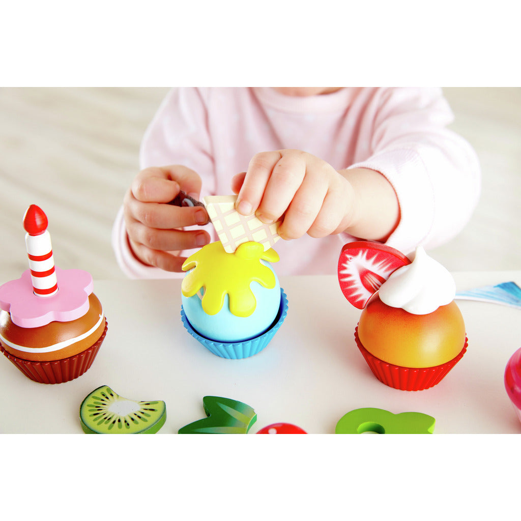 Child plays with wooden toy cupcakes, placing a waffle topping on the blue dessert