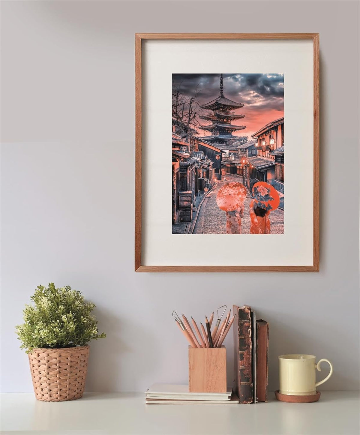 A framed photo of a Japanese street with a pagoda and two people with umbrellas at sunset, above a desk.