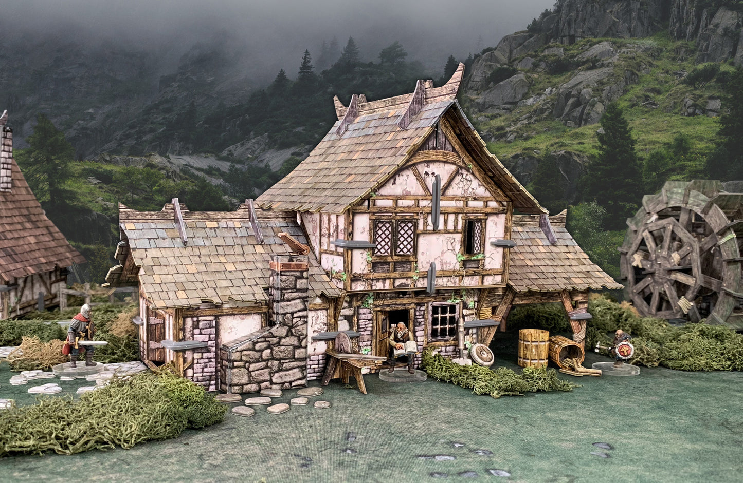 A detailed miniature fantasy village diorama featuring a timber-framed house, a reading figure, warriors, and a water wheel.