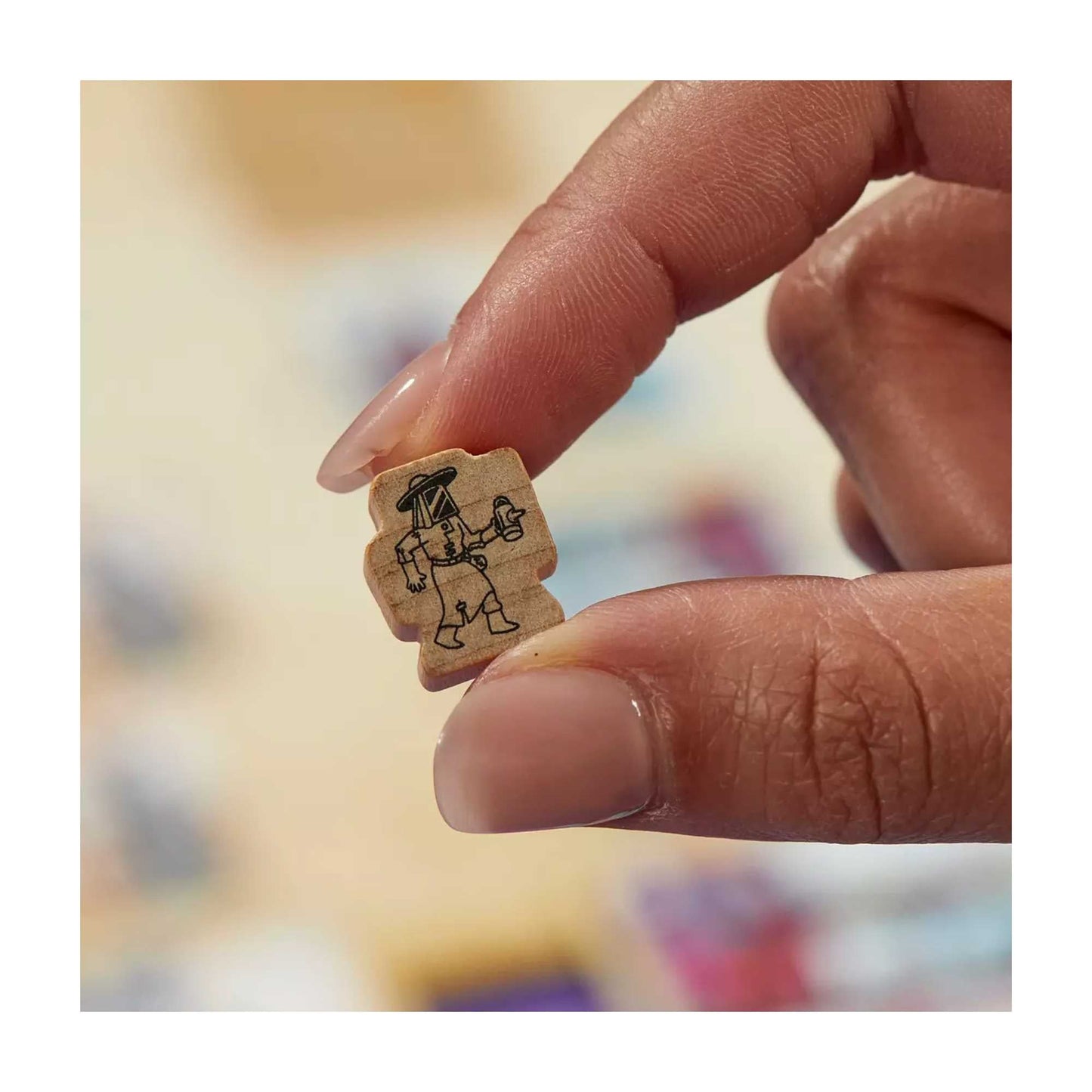 Hand holding a small wooden game token etched with a character in a protective suit and hat