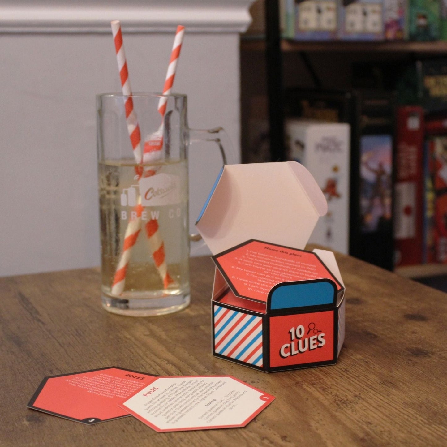 Open "10 Clues" game box, cards, and a drink with striped straws on a wooden table