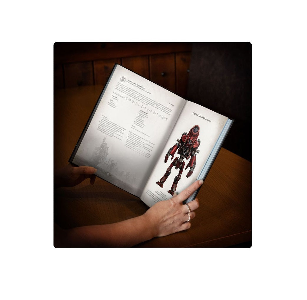 Hands hold an open book on a wooden table, showing game rules and a vibrant illustration of a red bipedal mech