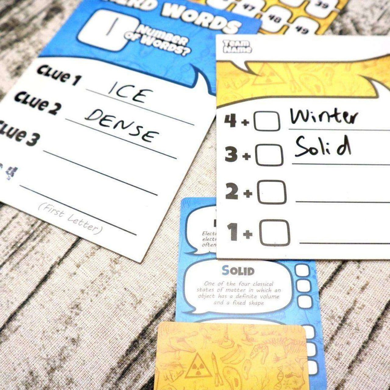 Game cards on a table, one showing clues 'ICE' and 'DENSE', another showing 'Winter' and 'Solid'