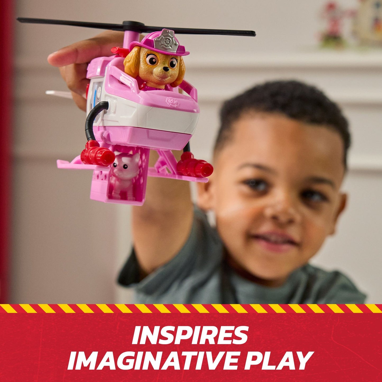 Child holds a pink Paw Patrol Skye helicopter toy with a dog figure and a small pig in a rescue cage