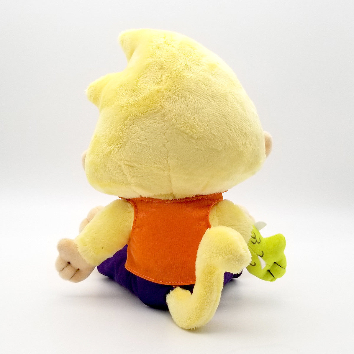 Yellow plush toy with spiky head, orange shirt, purple pants, and a tail, holding a small green creature, viewed from behind