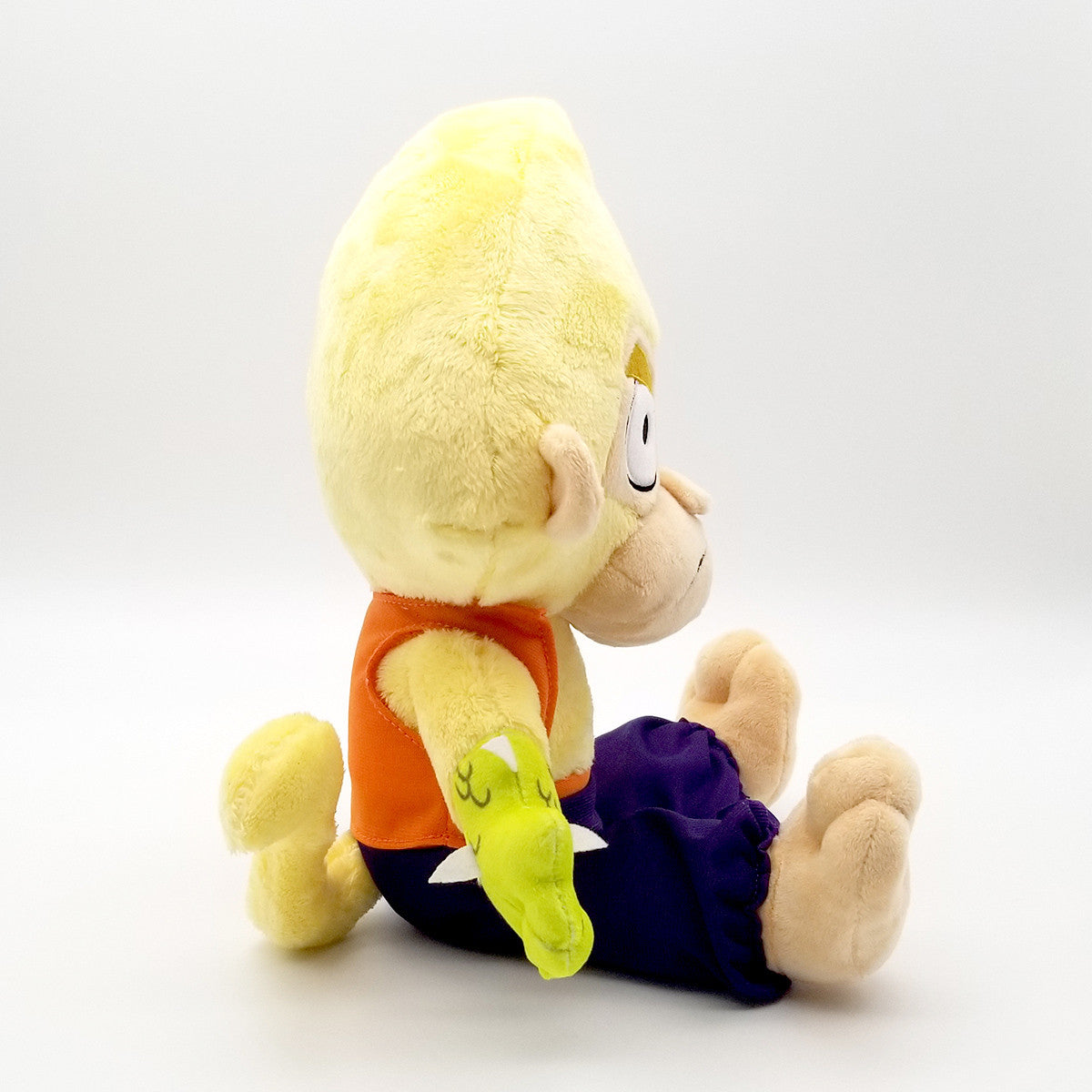 Yellow plush character wearing orange top and blue pants, with a green dragon arm accessory, sitting sideways