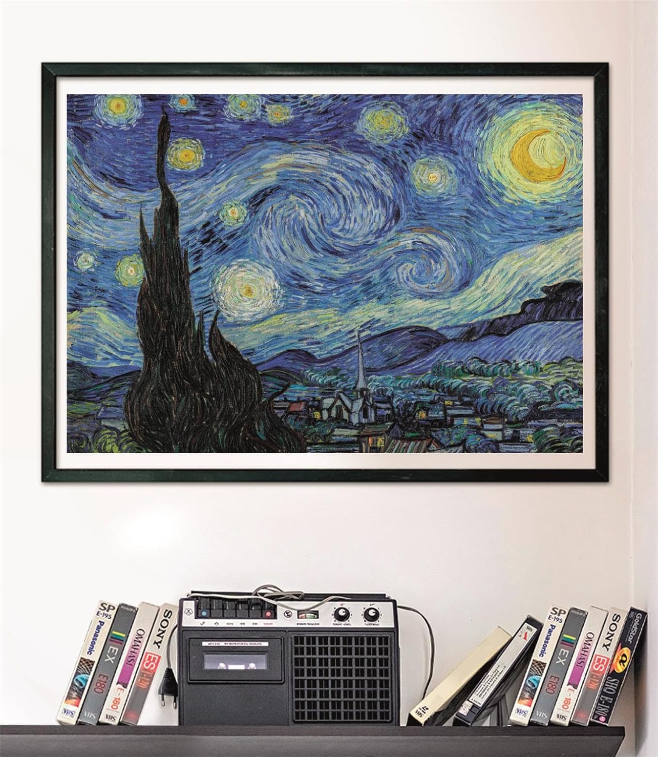 A framed Van Gogh's Starry Night print on a white wall above a vintage cassette player and VHS tapes on a shelf