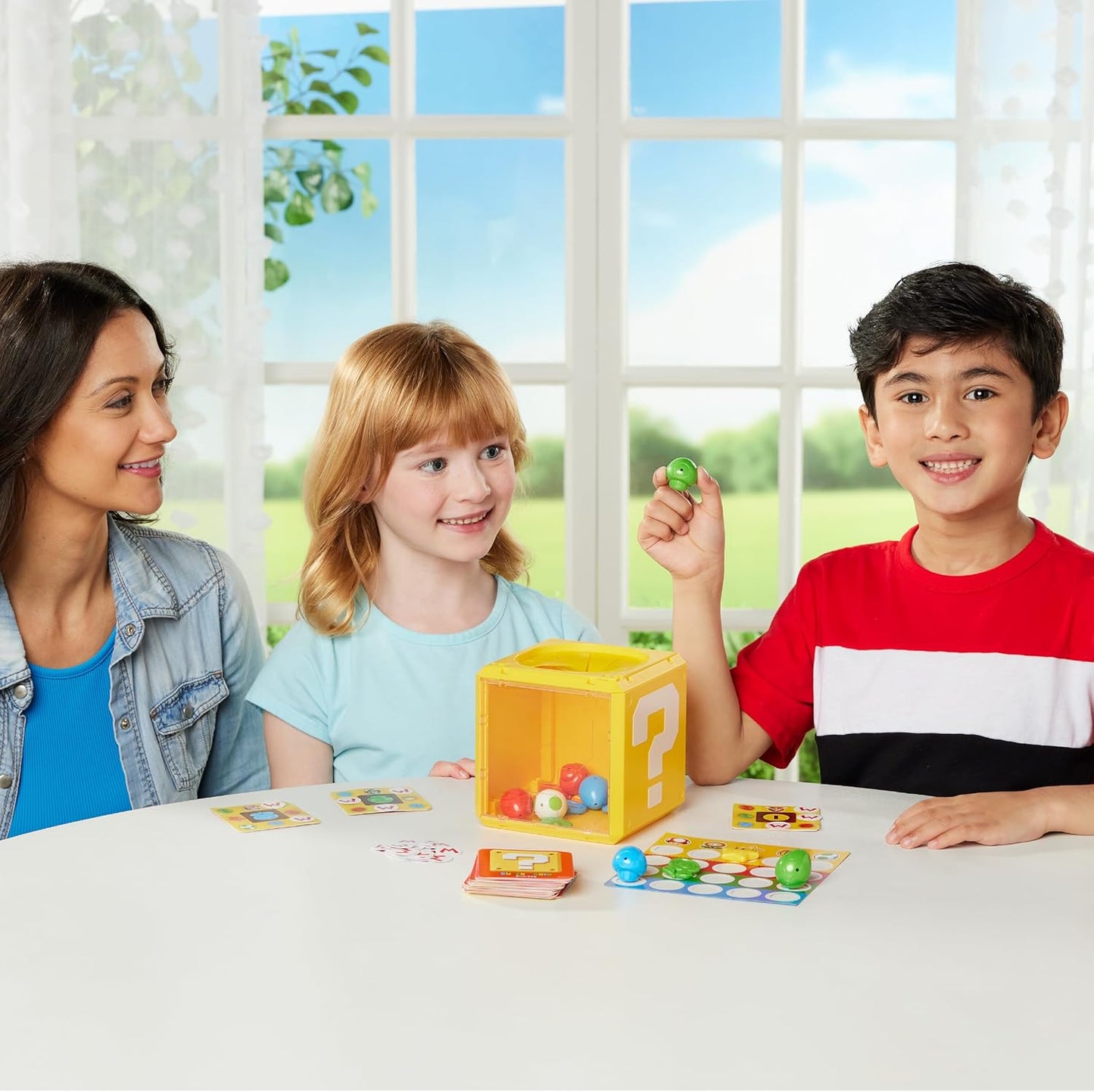 Three people smiling while playing a tabletop game featuring a yellow question block and small figures