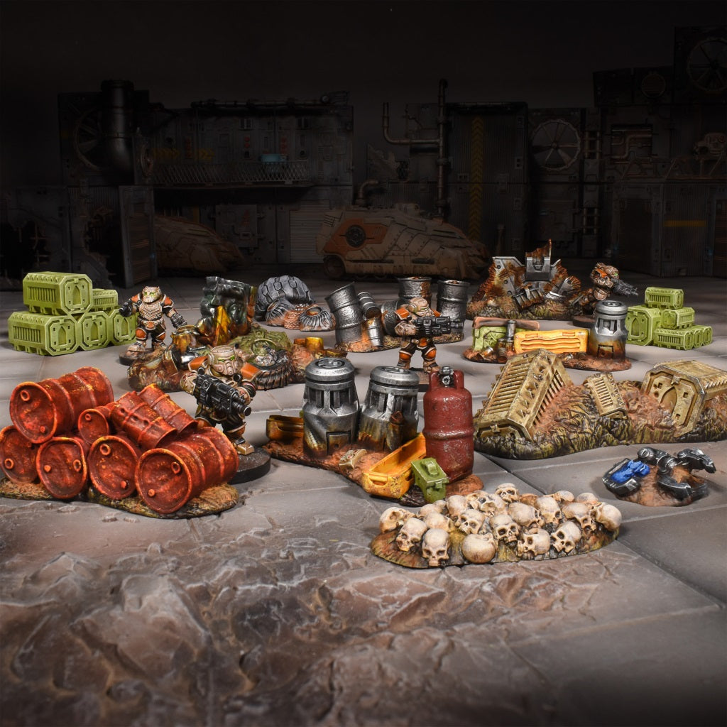 Painted miniature wargaming scene with armed soldiers amidst industrial scrap, crates, barrels, and a pile of skulls