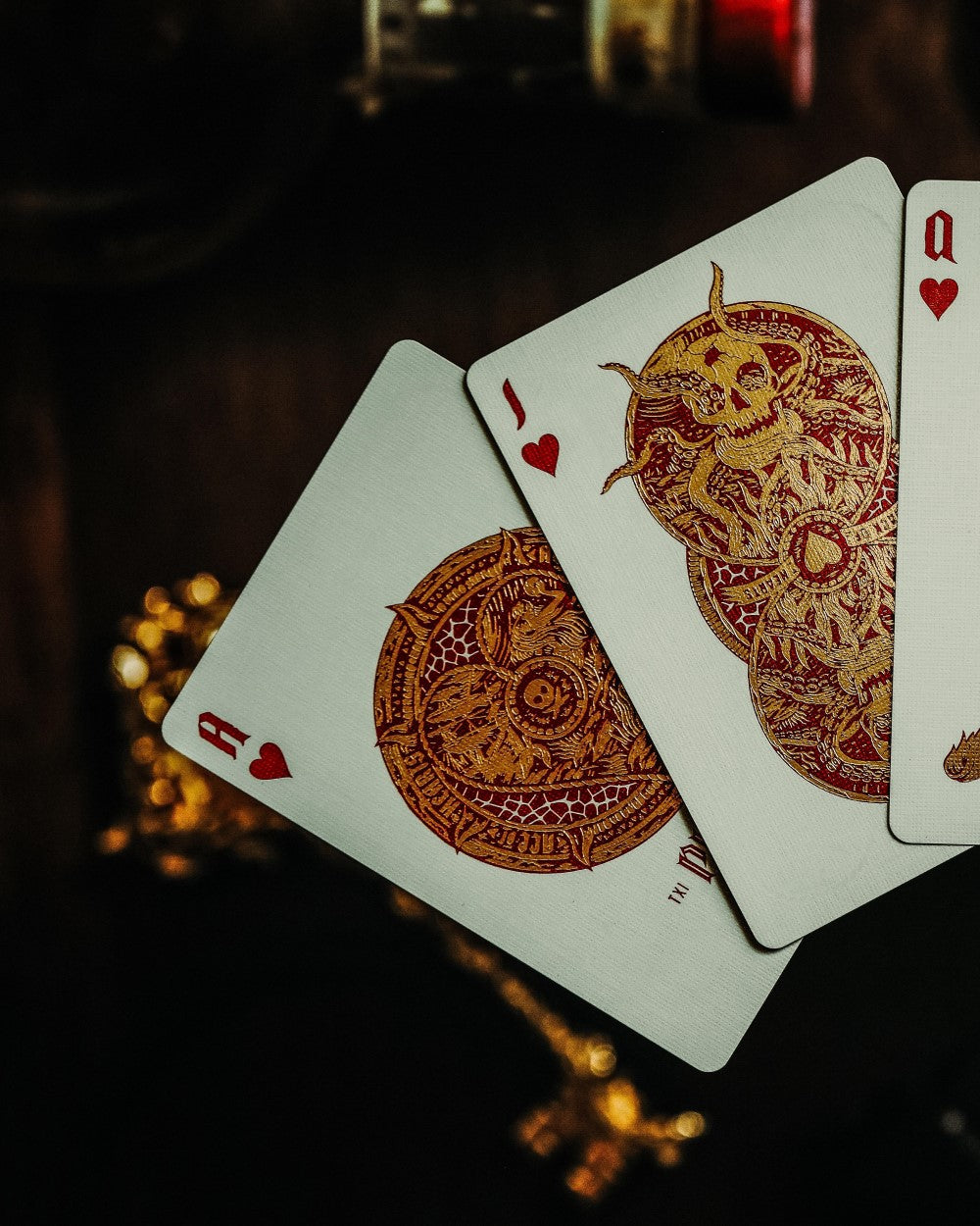 Ornate Ace, Jack and Queen of Hearts playing cards featuring detailed red and gold custom artwork in moody lighting