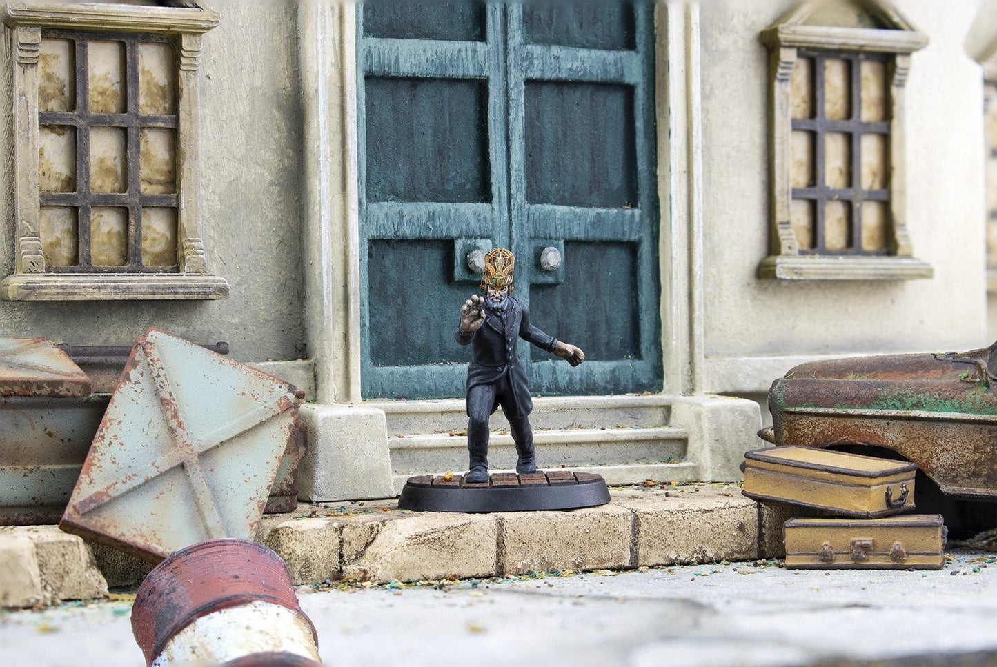 A miniature man in a dark suit and ornate gold headdress reaches forward on stone steps before a weathered building