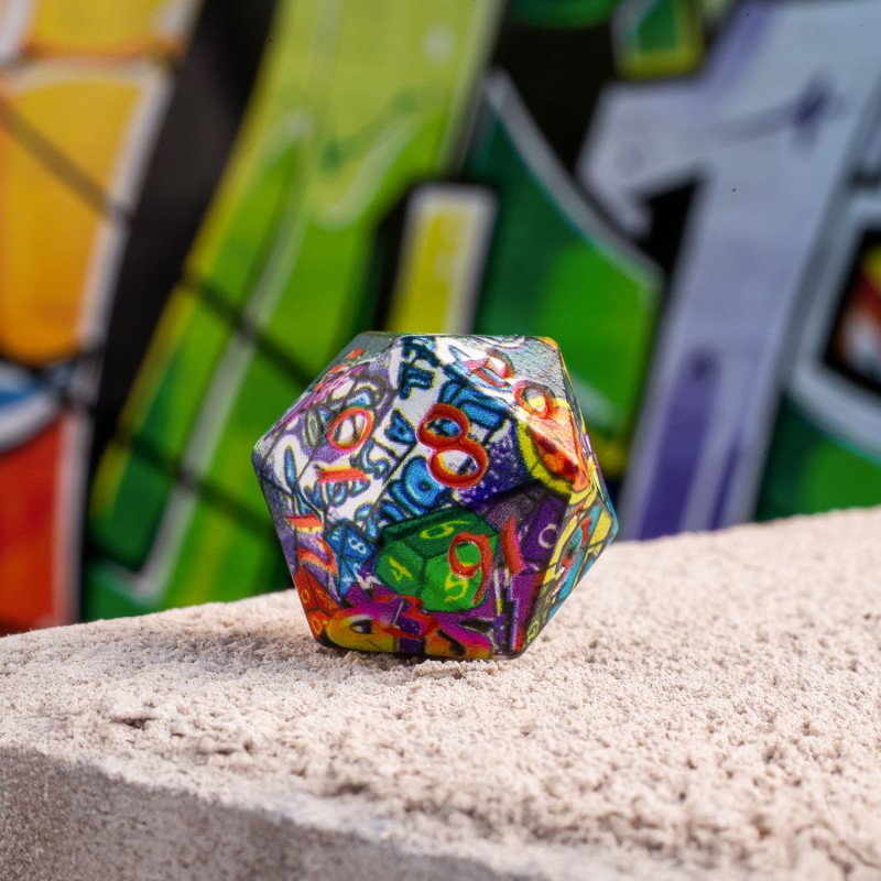 A colorful D20 die, a collage of dice and numbers, rests on a rough block before a blurred graffiti wall