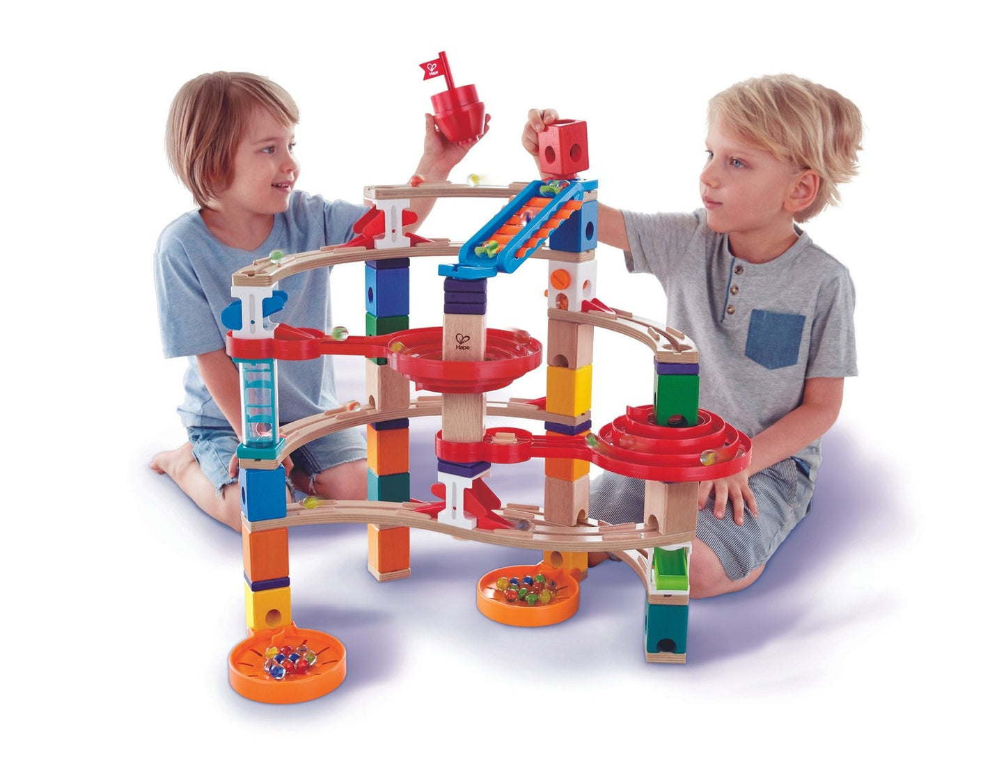 Two boys actively playing with a large, multicolored wooden marble run toy, feeding marbles into the tracks