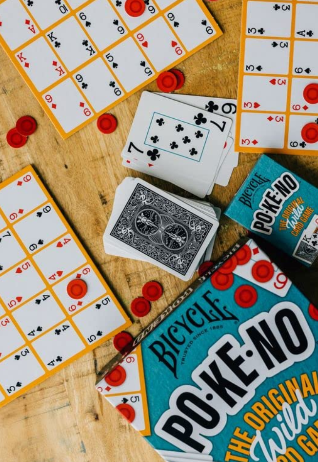 Bicycle Po-Ke-No game spread on a wooden table with cards, unique boards, red chips, and the game box