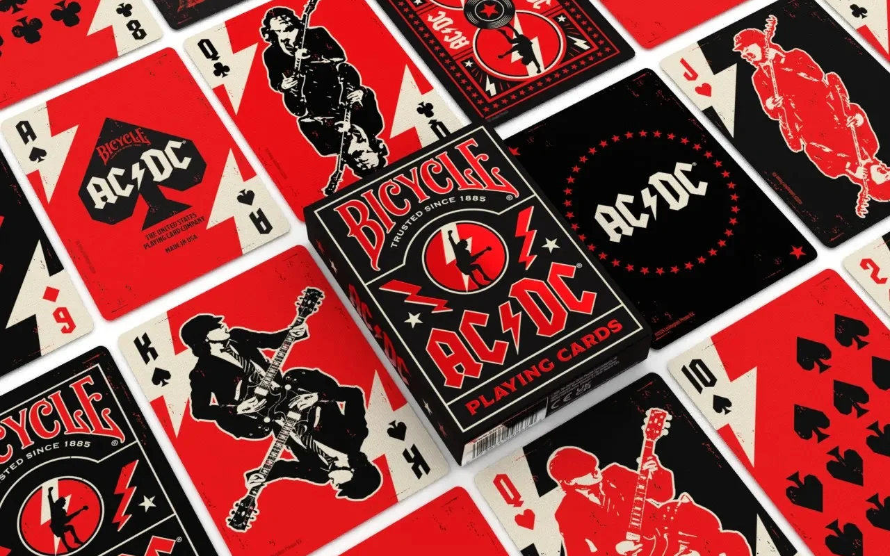 Close-up of black and red Bicycle AC/DC playing cards and their tuck box scattered on a surface