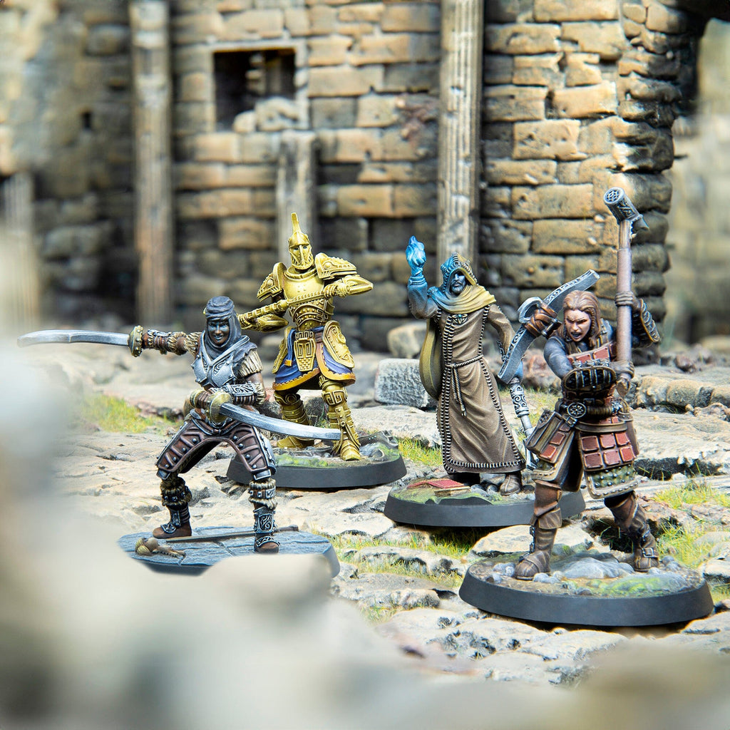 Four fantasy miniatures: a dual-wielding fighter, golden warrior, wizard with blue magic, and a warrior, posed amidst ruins