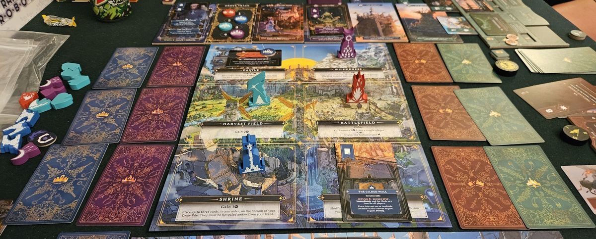 Tabletop view of a fantasy strategy game setup, showing a modular game board, several decks of cards and wooden player pieces