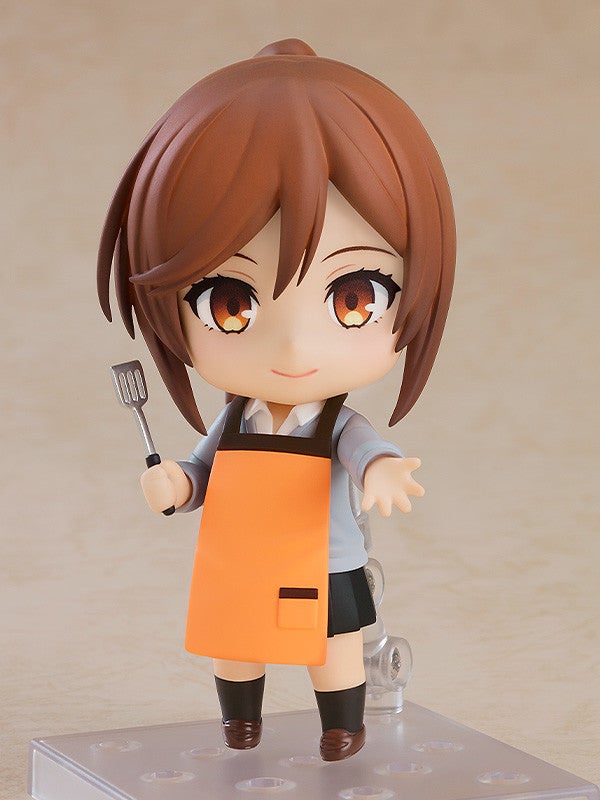 Nendoroid figure of a girl with brown hair orange apron and black skirt holding a spatula
