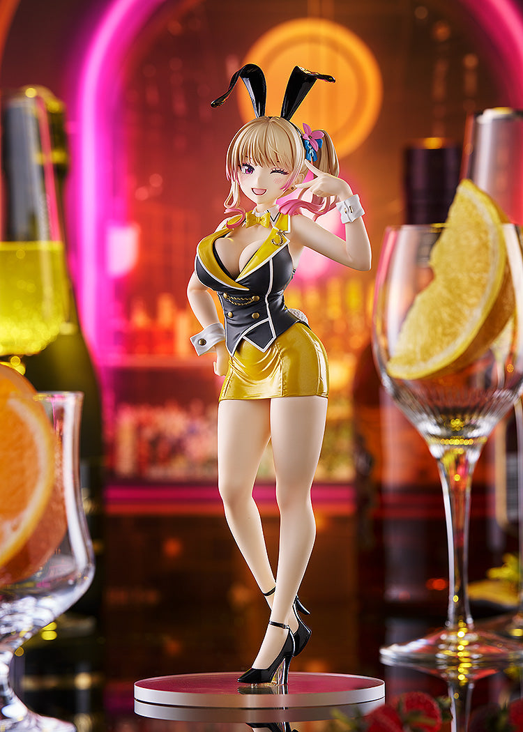 Blonde anime figurine with bunny ears and black-gold outfit, winking and pointing in a neon-lit bar