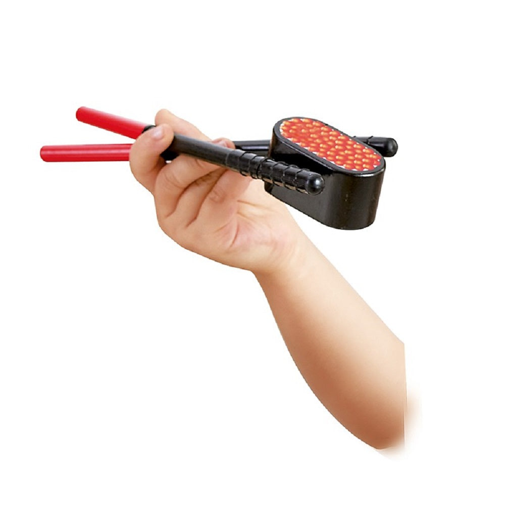 Child's hand holds a toy chopstick training device: black handle, red tips, and a block topped with faux beans