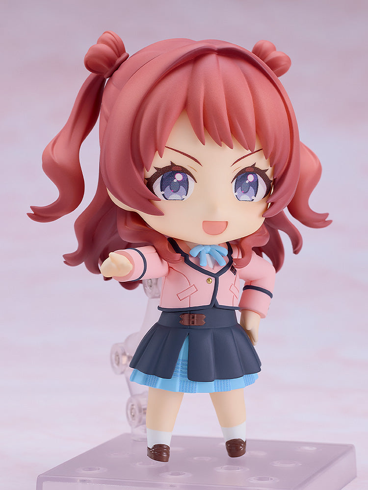 A Nendoroid Saki Hanami figure with pink pigtails, blue eyes, and a cheerful smile, wearing a pink jacket and blue school skirt, standing on a clear display base