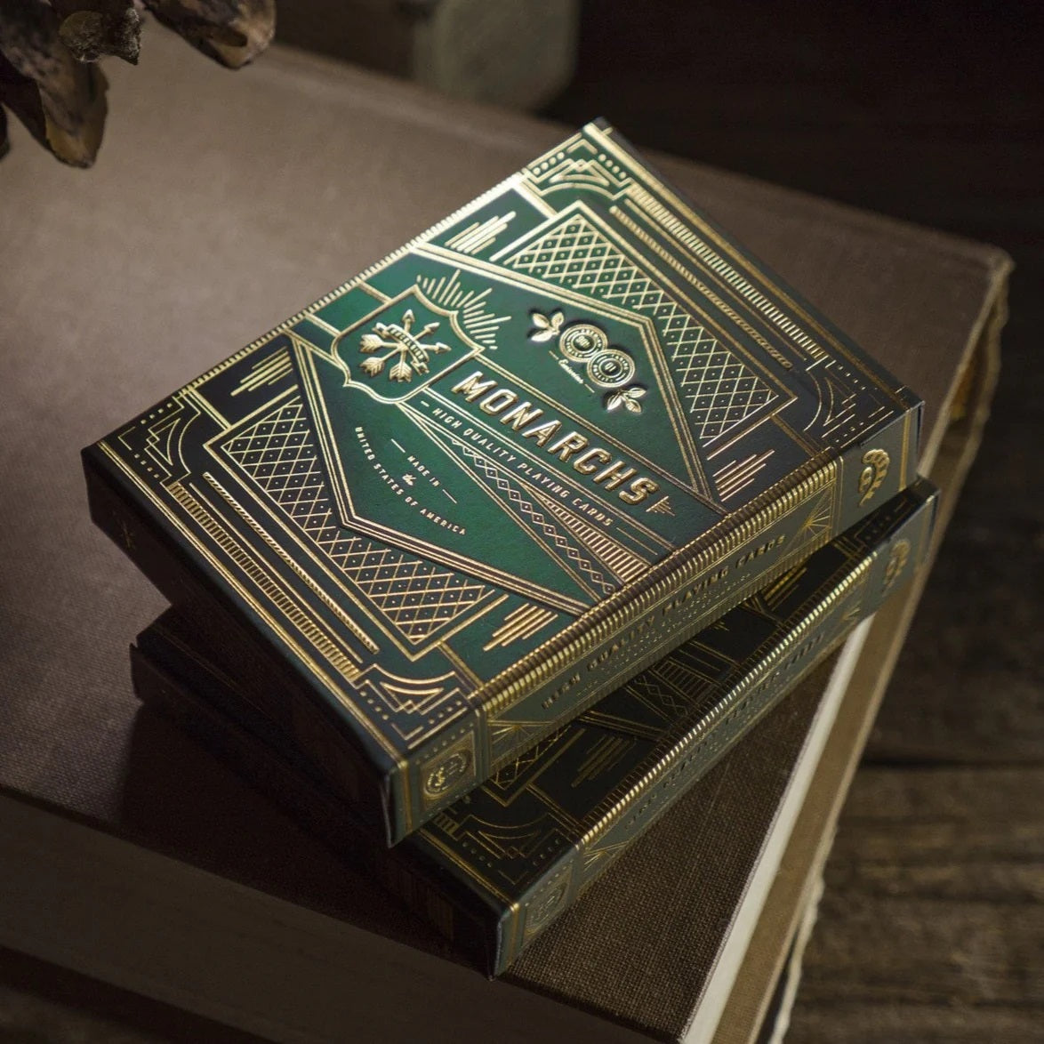 A dark green and gold Monarchs playing card box with ornate designs, resting on old books
