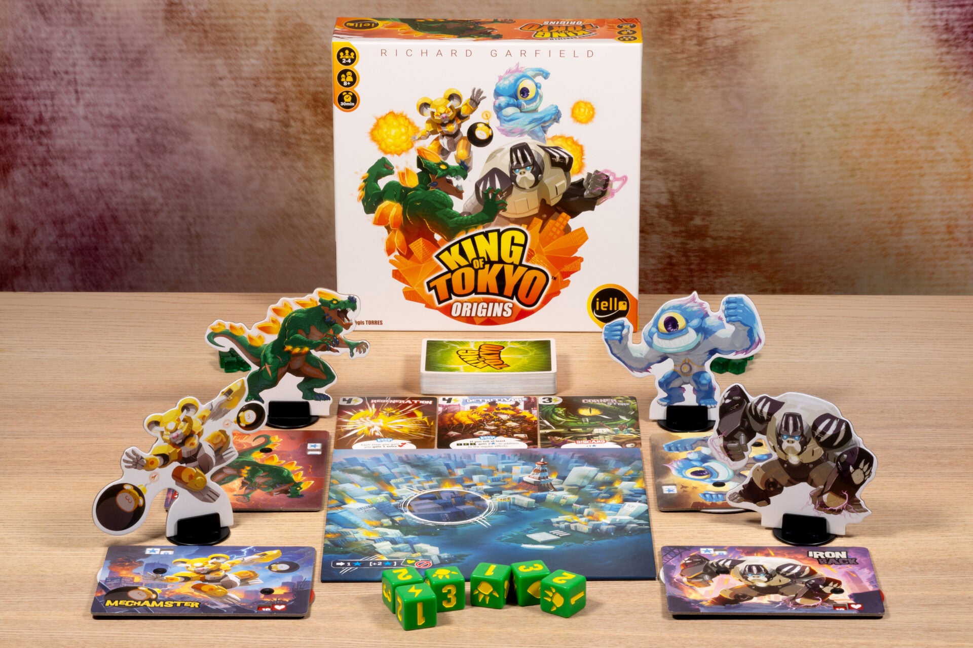 King of Tokyo: Origins board game setup featuring its box, city board, colorful monster standees, character cards, and green dice.