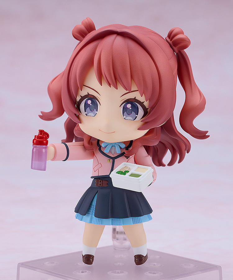 A Nendoroid Saki Hanami figure with pink pigtails, a pink jacket, and a blue skirt holds a purple water bottle in one hand and a white bento box in the other