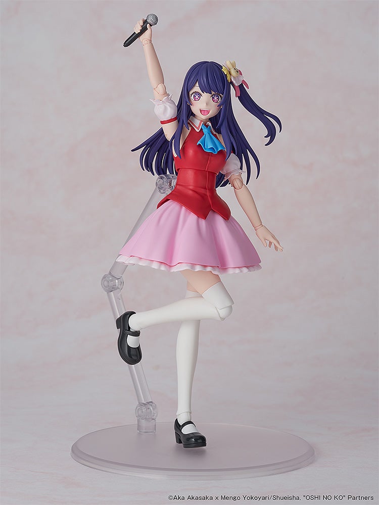 An articulated anime figure with purple hair, red top, pink skirt, holding a microphone overhead, smiling