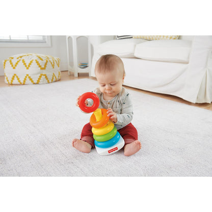 A baby sits on a rug -  holding a red ring and stacking colorful rings on a Fisher-Price toy