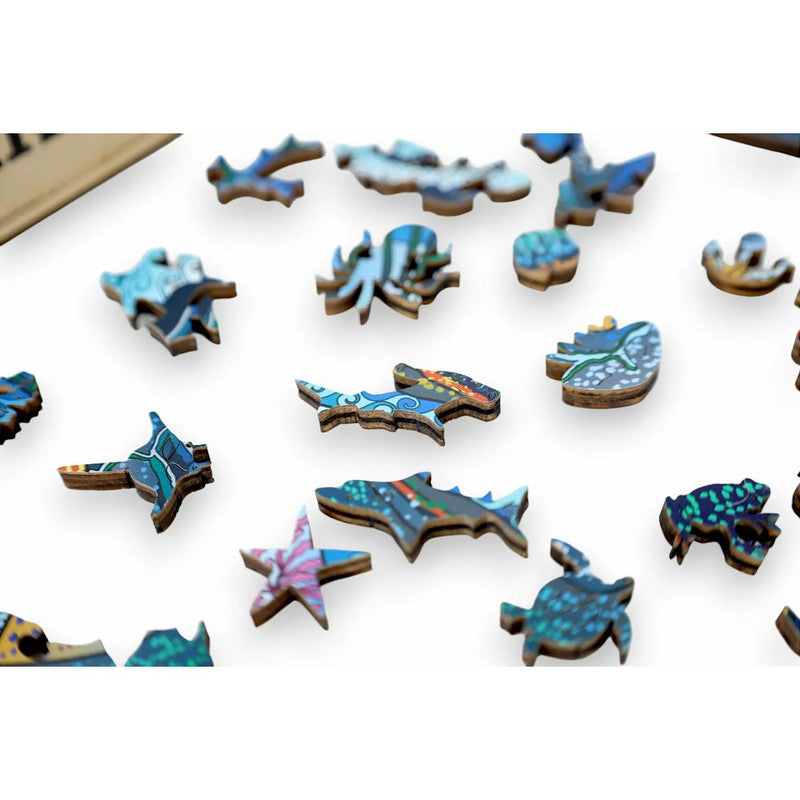 Scattered wooden jigsaw puzzle pieces, vividly coloured and shaped like various sea animals, on a white surface