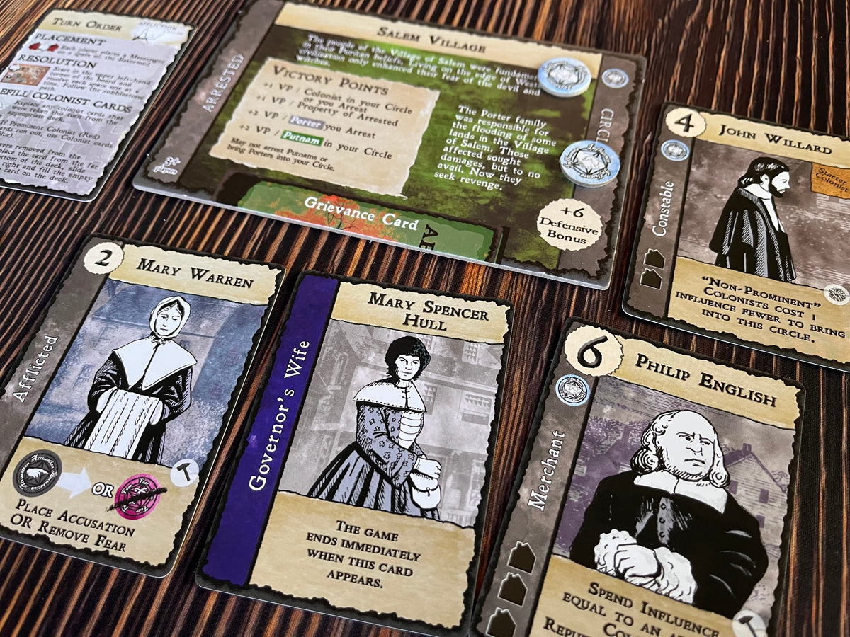 A close-up of game cards from the Salem Village board game Features character cards with colonial illustrations, rules, and game tokens