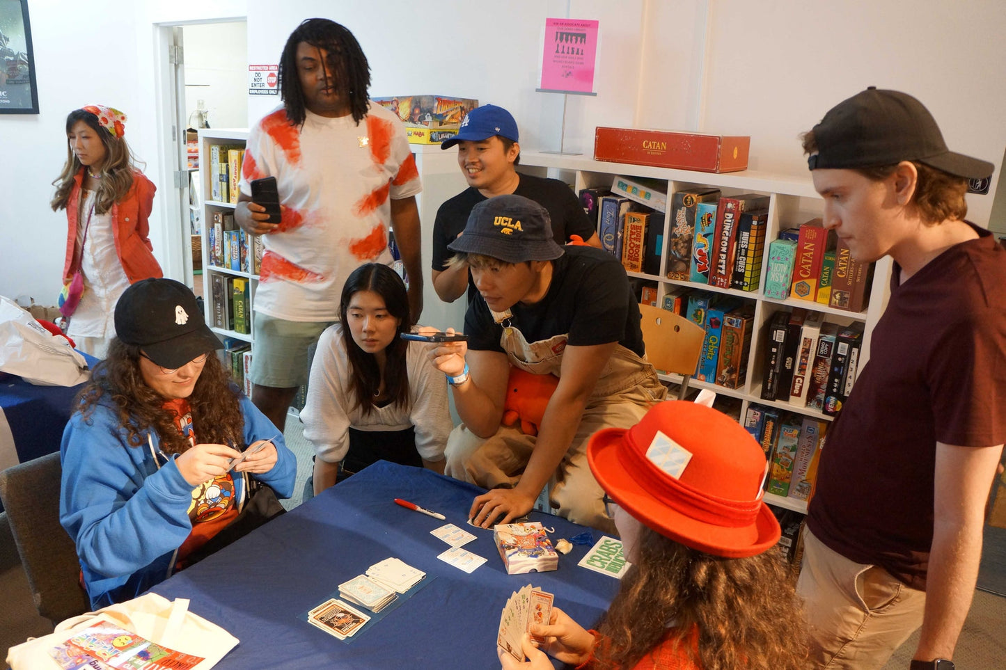 A diverse group of young adults plays Crabs in a Bucket card game at a blue table