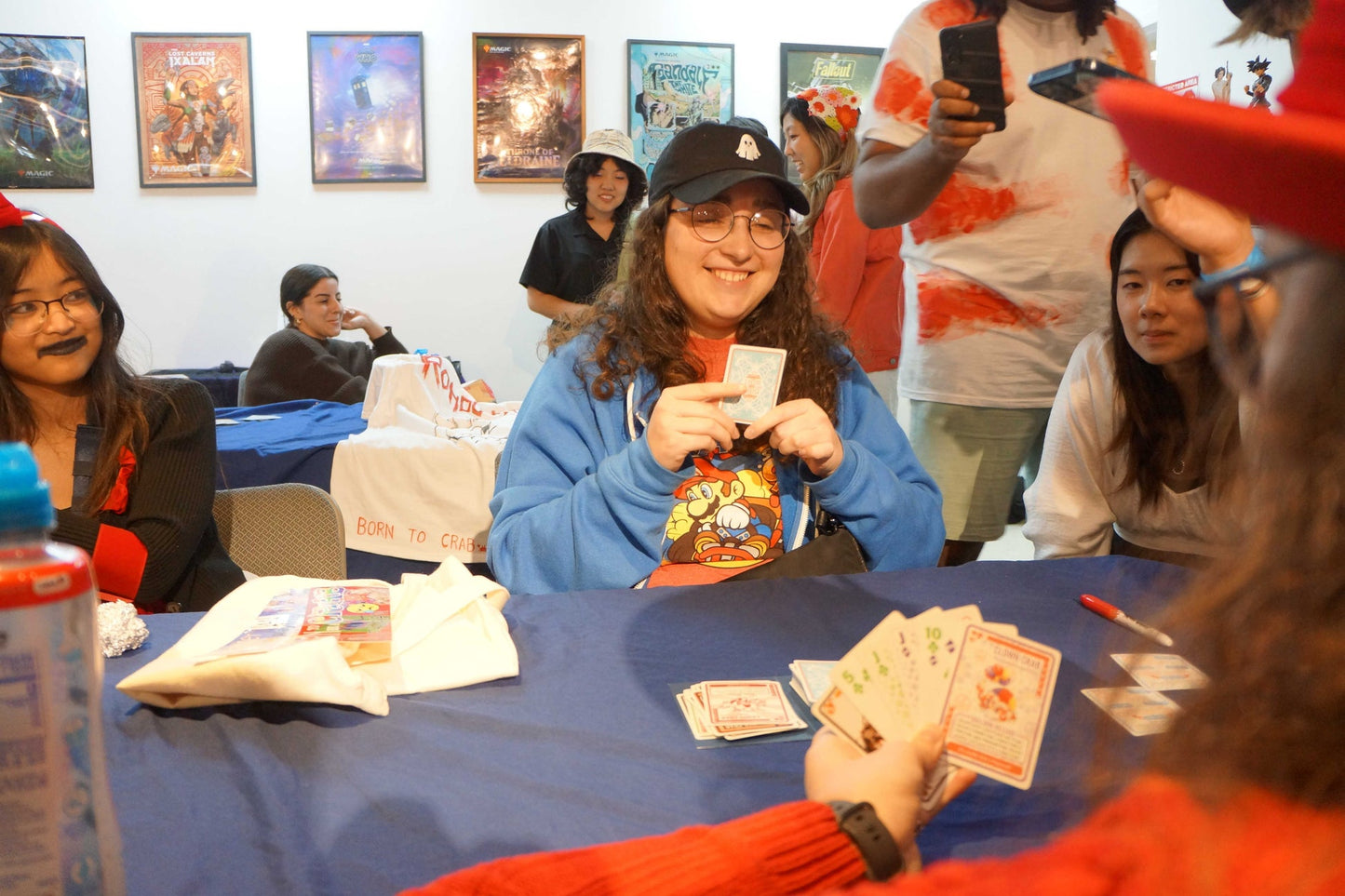 Smiling person in a ghost cap plays Crabs in a Bucket card game at a table with others