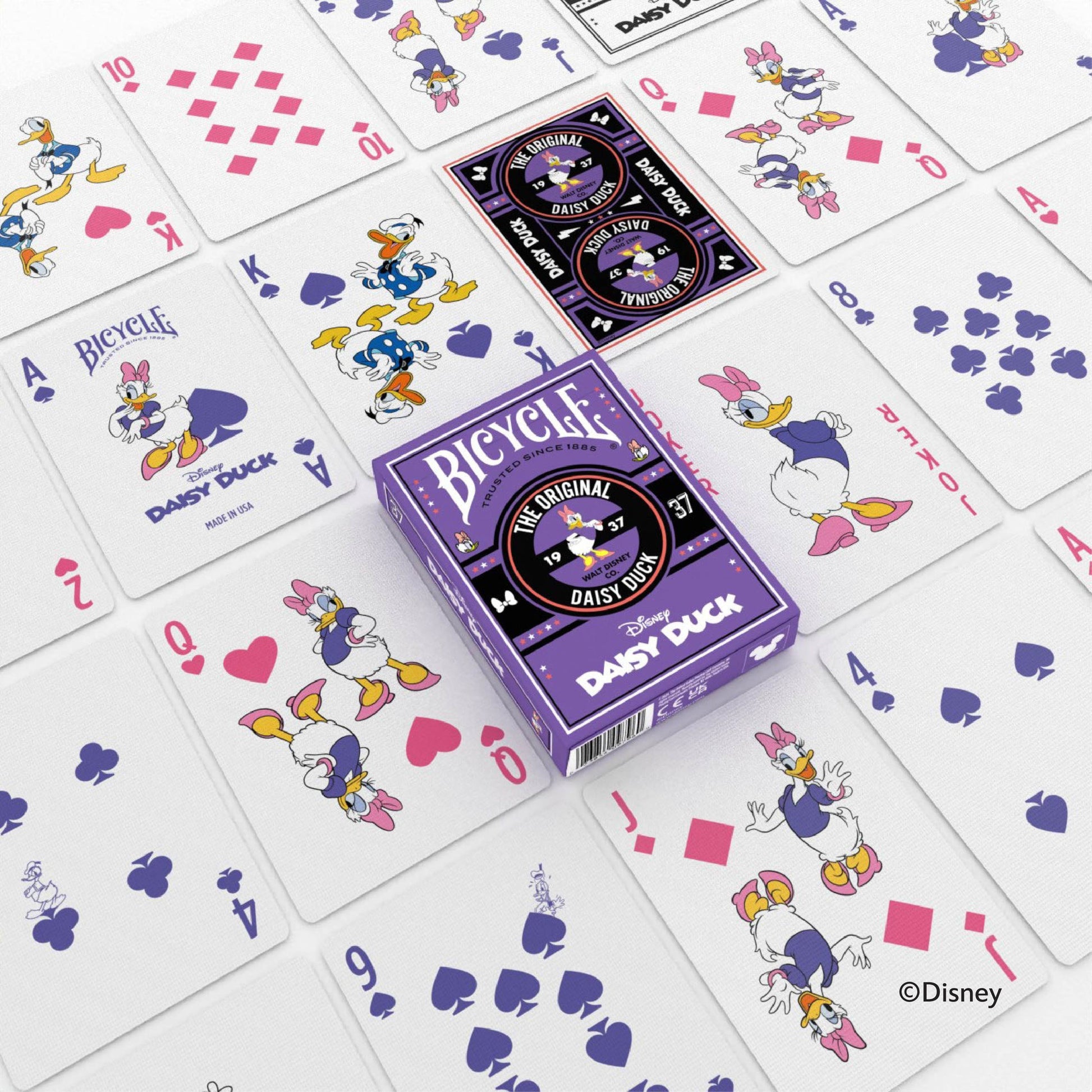 A purple Bicycle Disney Daisy Duck playing card box surrounded by many scattered cards featuring Daisy and Donald Duck artwork