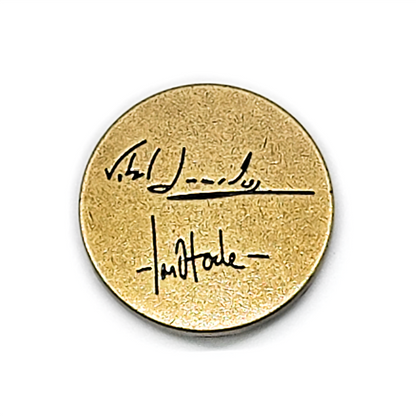 Round antique gold coin with black handwritten signature and underline across the center