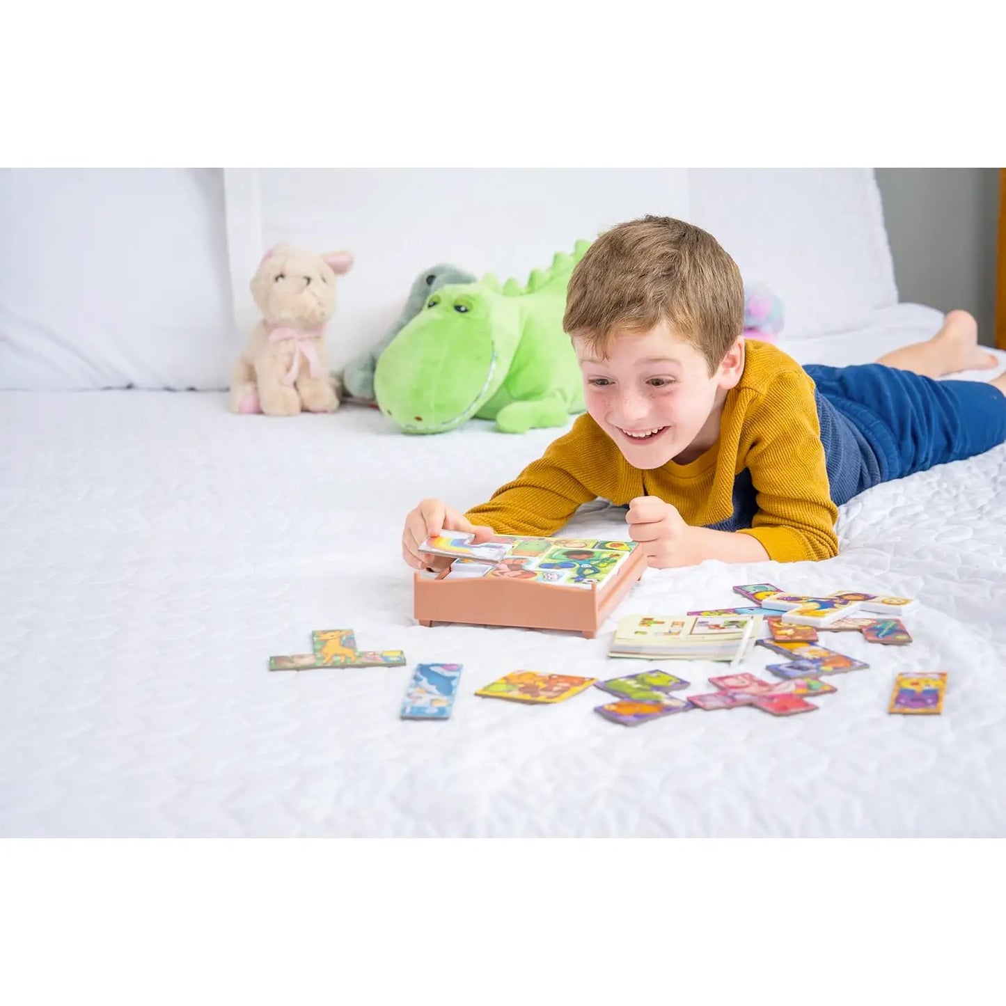 Smiling boy playing a card matching game on a white bed with stuffed toys